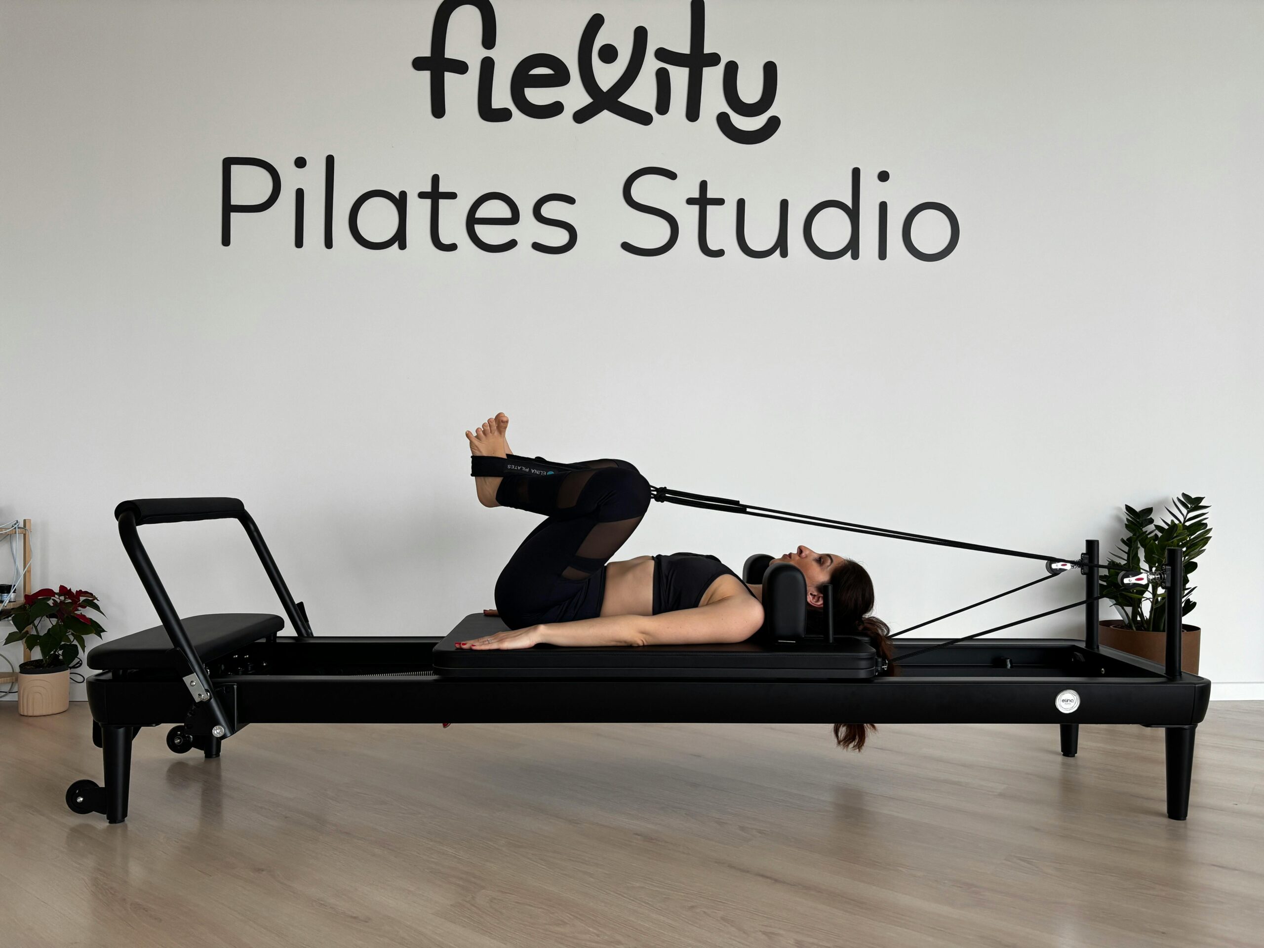 Frau praktiziert Pilates auf einem Reformer-Gerät in einem modernen Studio.