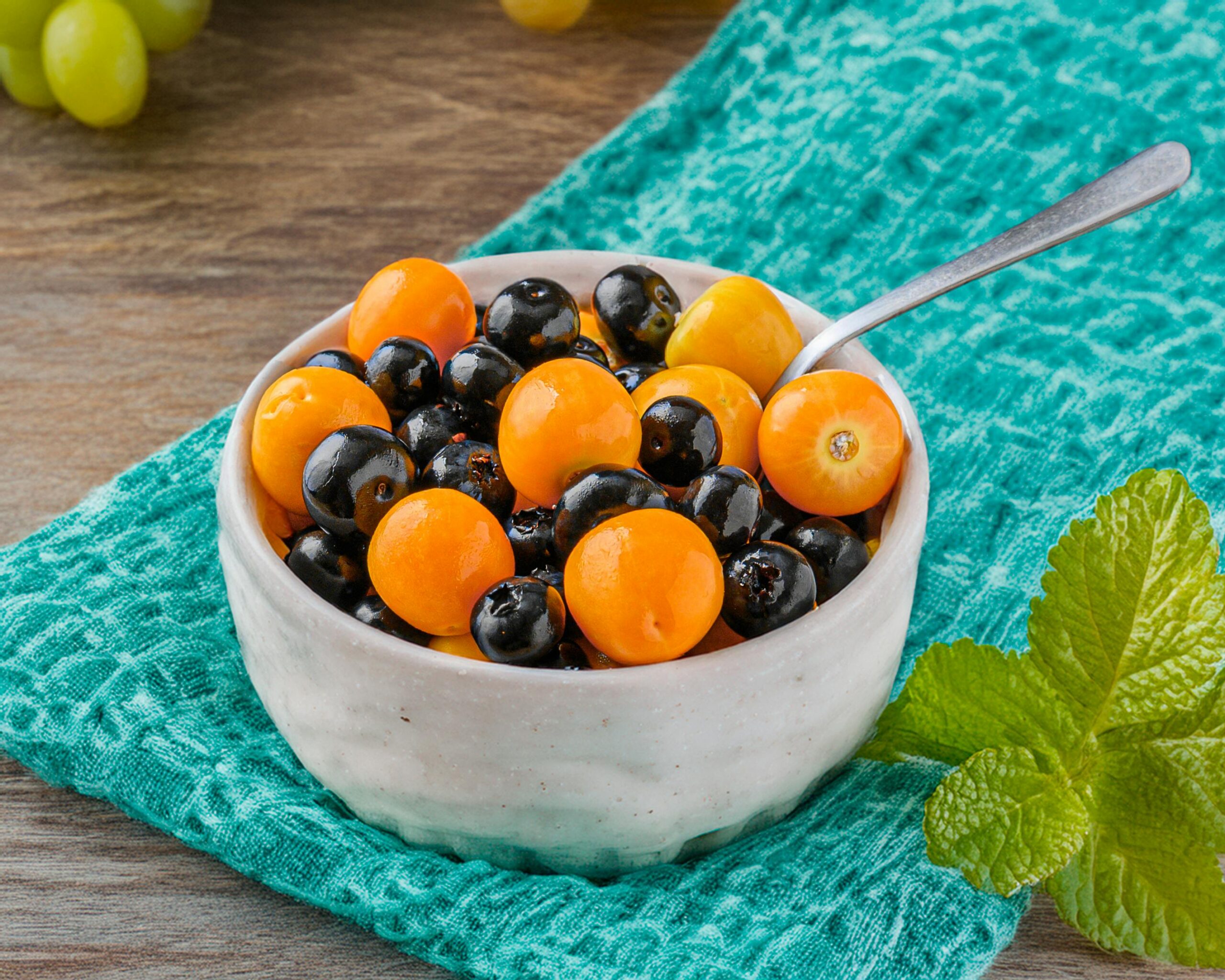 Leuchtend bunte Schale mit frischen Orangen- und Brombeeren auf einem Holztisch mit blaugrünem Tuch.
