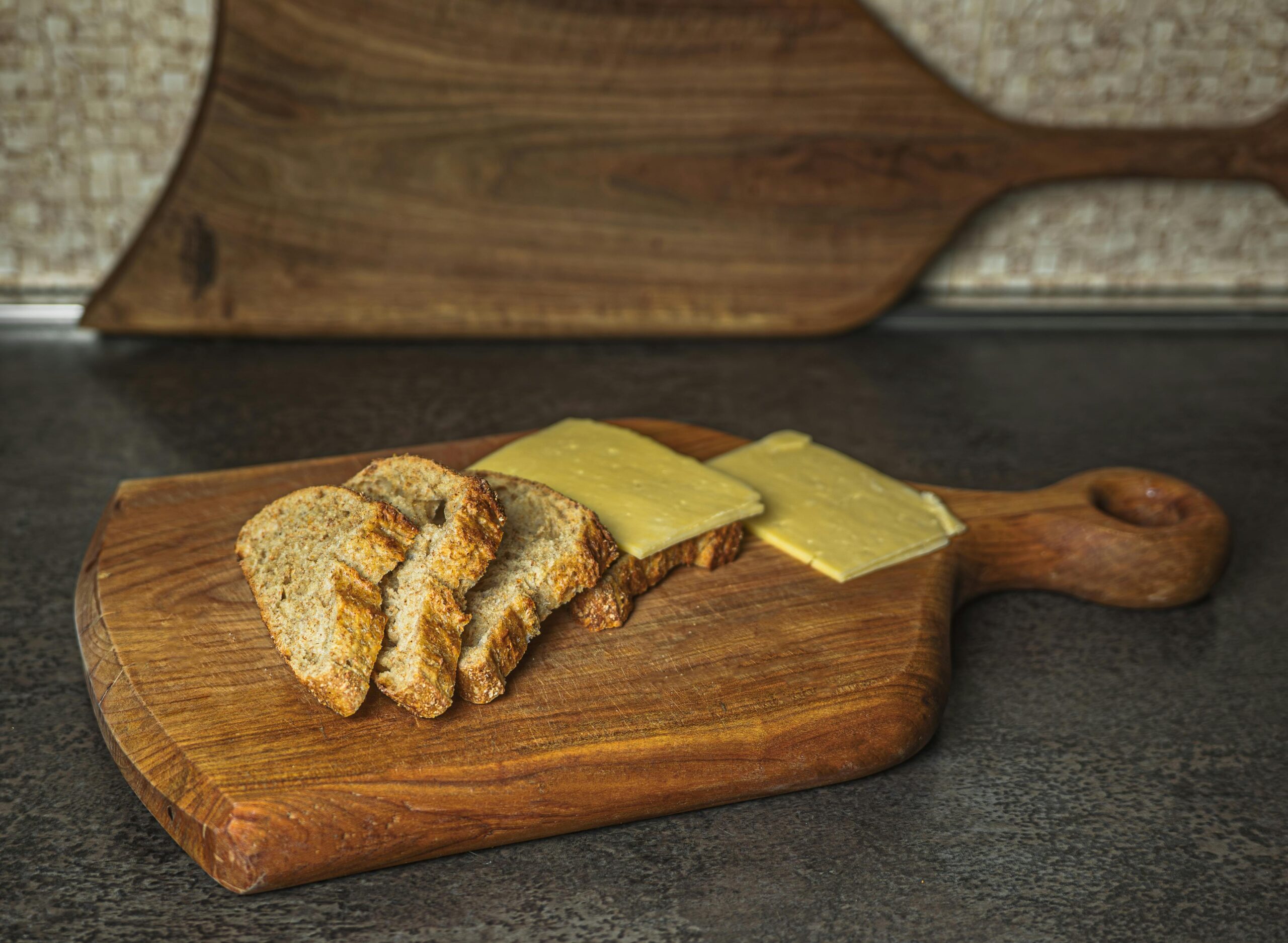 Geschnittenes rustikales Brot mit Käse auf einem Holzbrett, perfekt für ein einfaches kulinarisches Ambiente.