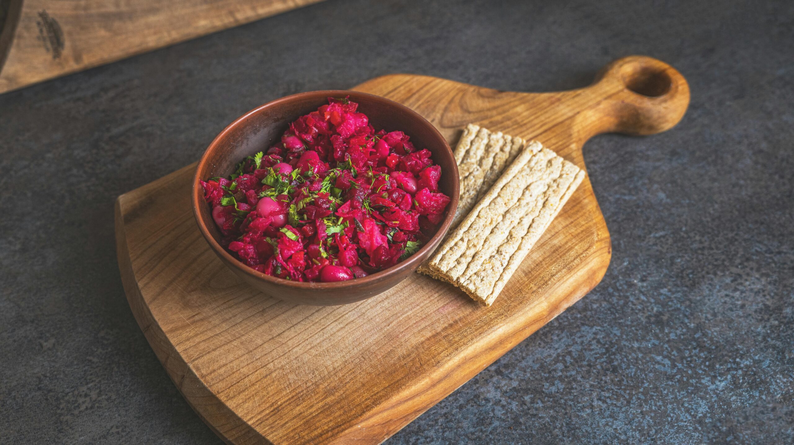 Ein farbenfroher Rote-Bete-Salat, serviert in einer Schüssel mit Roggencrackern auf einem Holzschneidebrett.