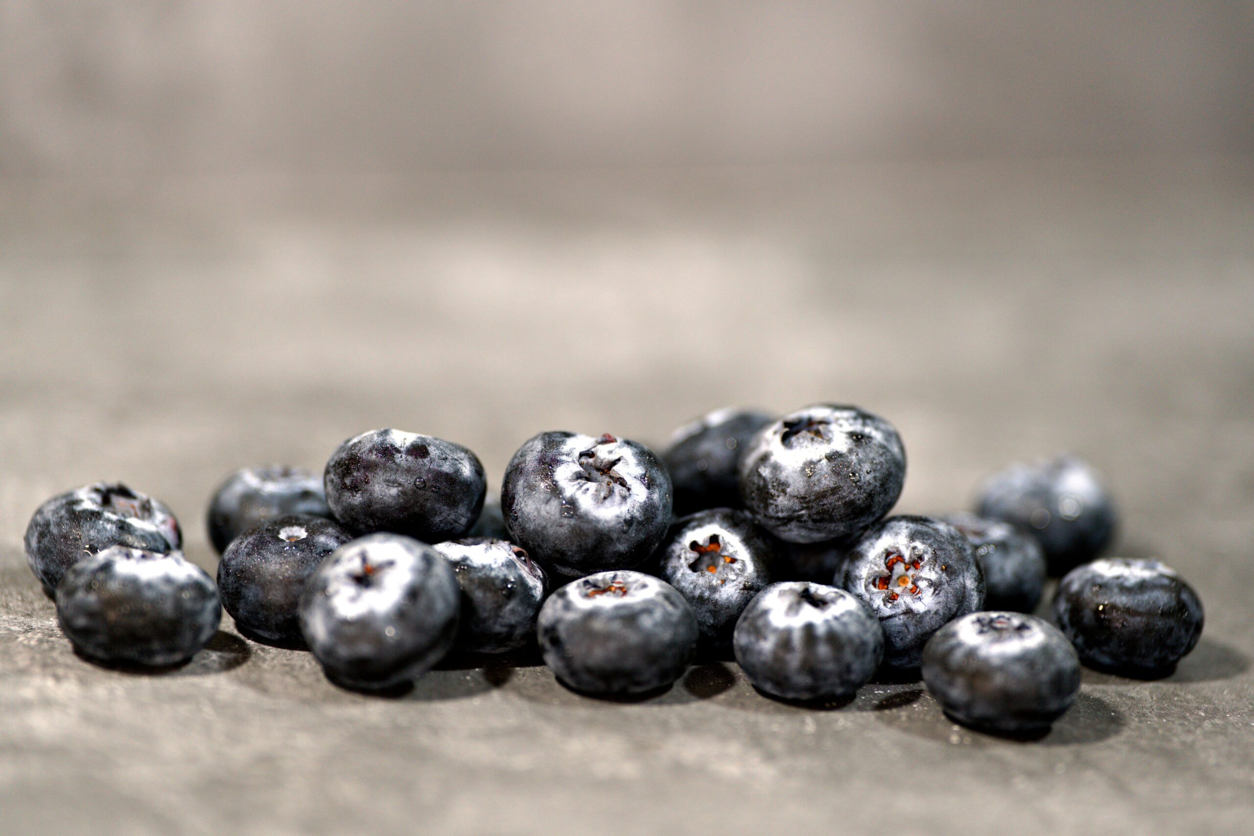 Eine Nahaufnahme von frischen Blaubeeren, die auf einer grauen Oberfläche verstreut sind.