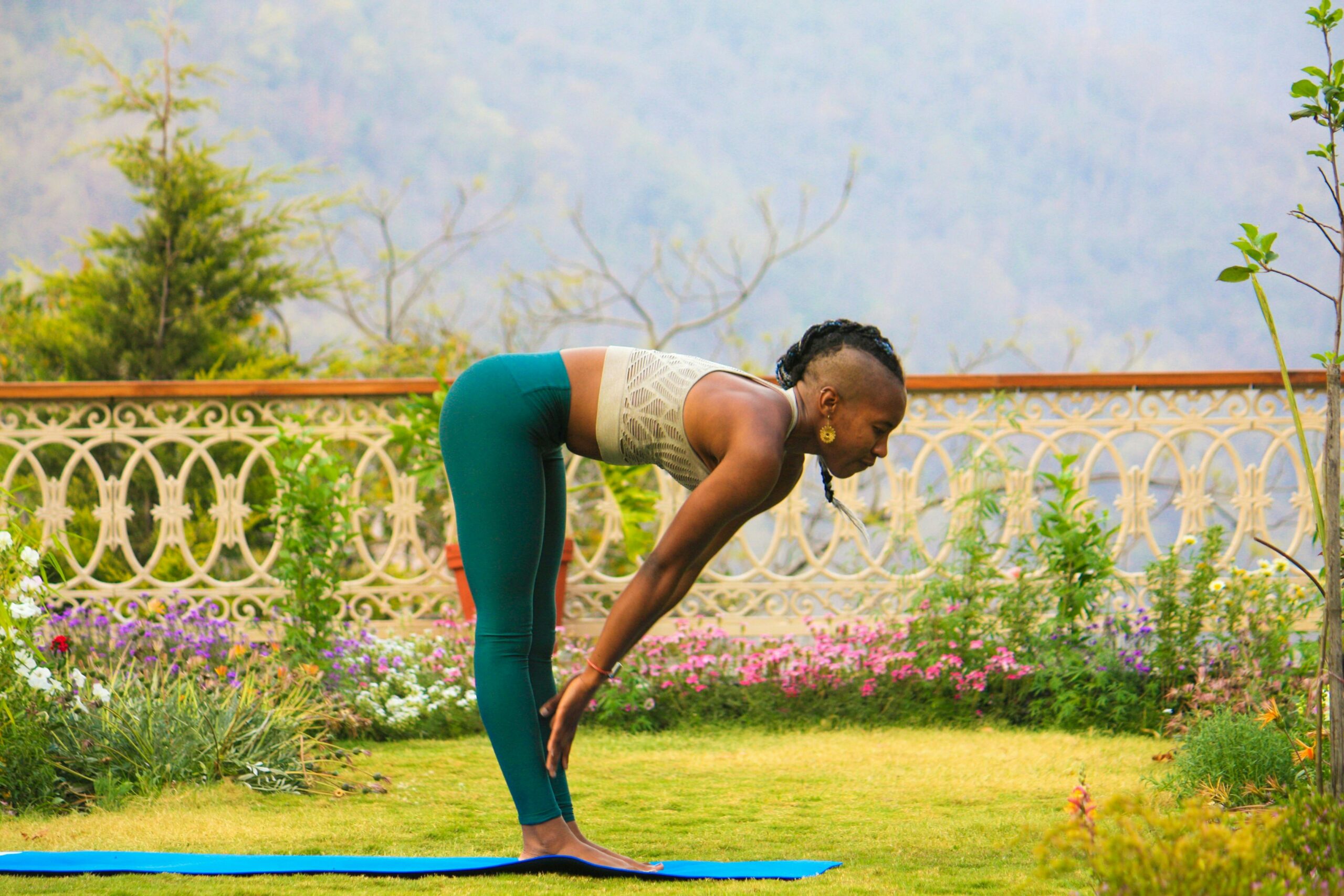 Eine Frau praktiziert Yoga im Freien in Rishikesh, Indien, umgeben von einem üppigen Garten und malerischer Aussicht auf die Berge.