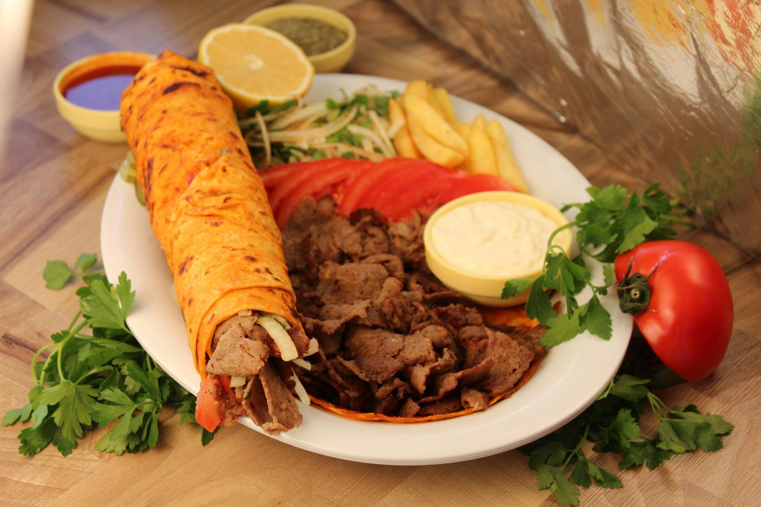 Appetitliches Shawarma aus dem Nahen Osten mit Lavash-Brot, Soßen und frischem Gemüse auf einem Teller.