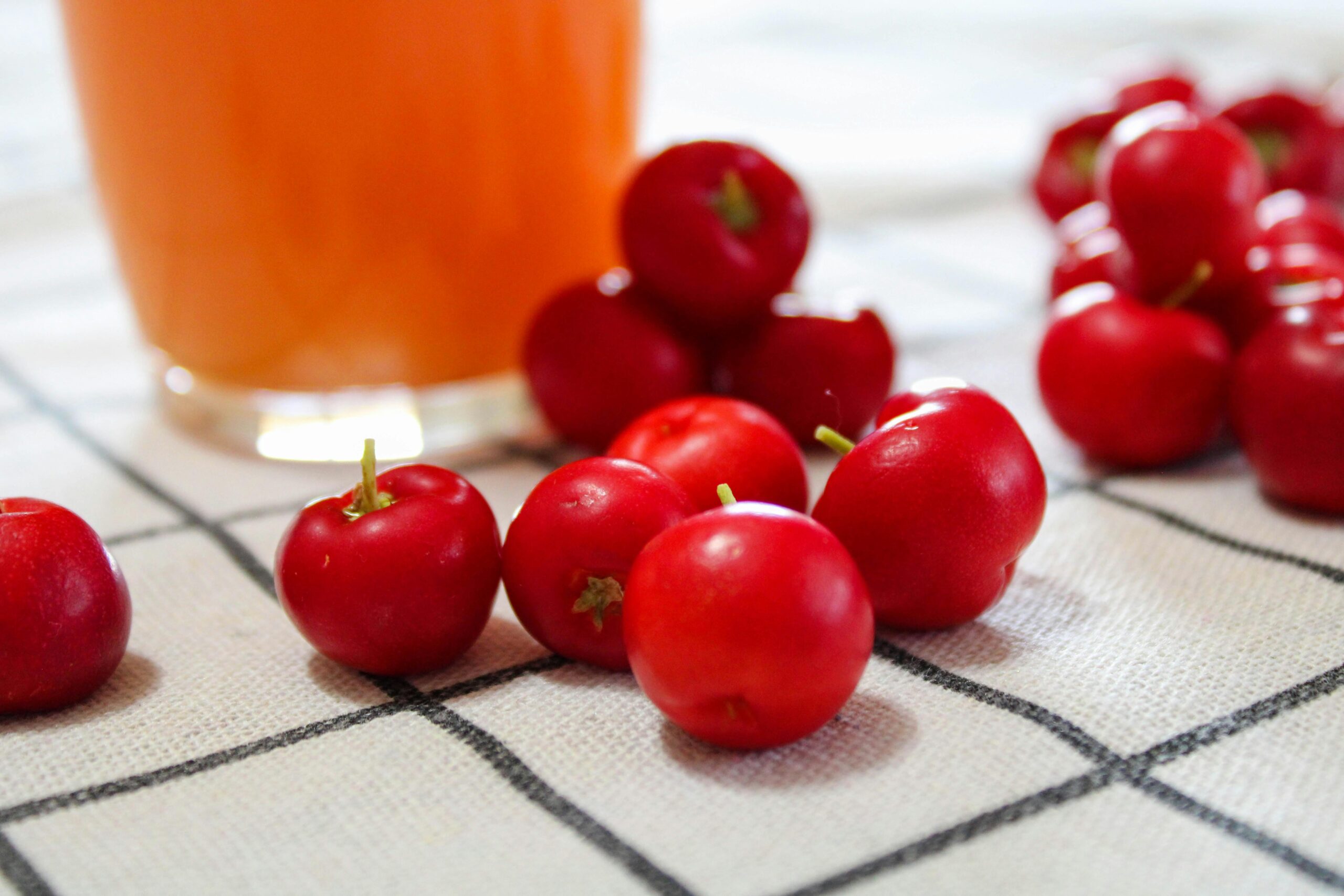Ein lebendiges Bild von Acerola-Kirschen und Saft auf einer karierten Tischdecke, das natürliche Erfrischung präsentiert.