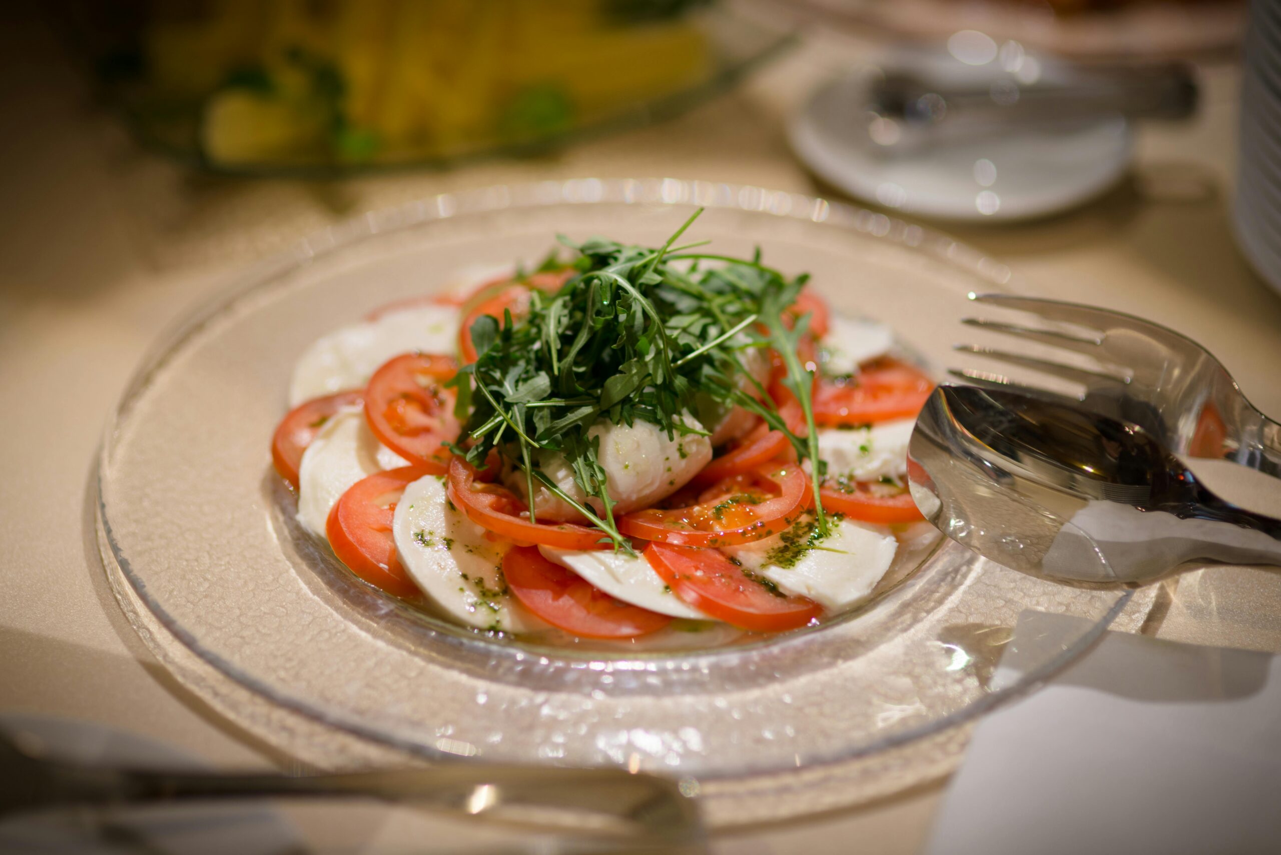 Frischer Caprese-Salat mit Mozzarella, Tomaten und Rucola auf einem Glasteller.