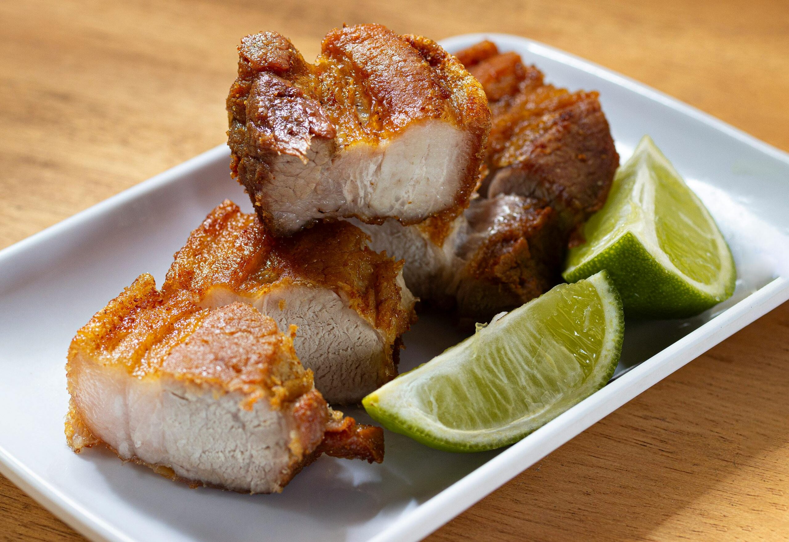 Leckerer knuspriger Schweinebauch, serviert auf einem Teller mit frischen Limettenspalten, perfekt für eine schmackhafte Mahlzeit.