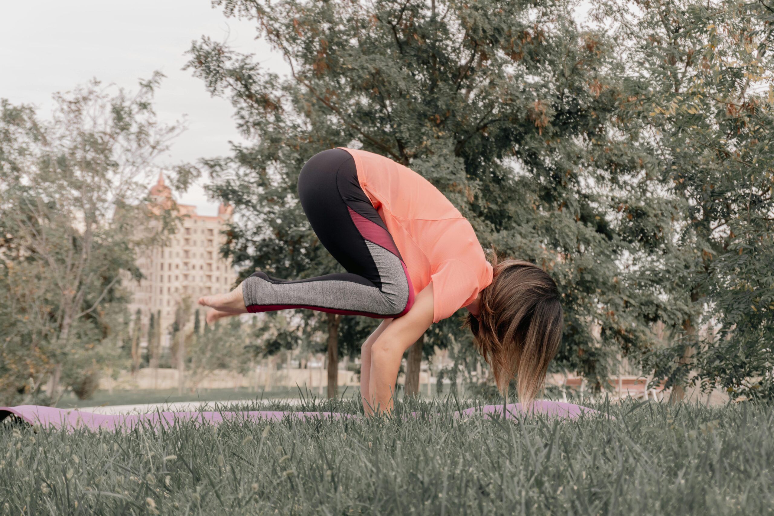 Eine Frau hält eine Yoga-Pose auf einer Matte in einem Park und demonstriert dabei Gleichgewicht und Konzentration.